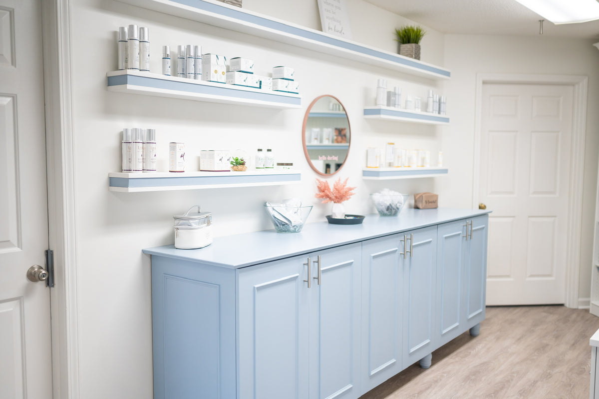 A light blue wooden medicine cabinet with matching floating shelves and countertop, styled in a bright, clean white clinic or home interior.
