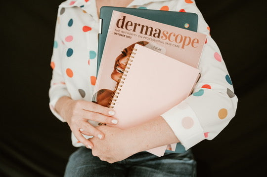 Person holding a magazine titled 'dermascope' and a notebook with a polka dot shirt.