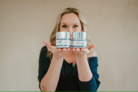 Person holding two jars of cream in front of a plain background