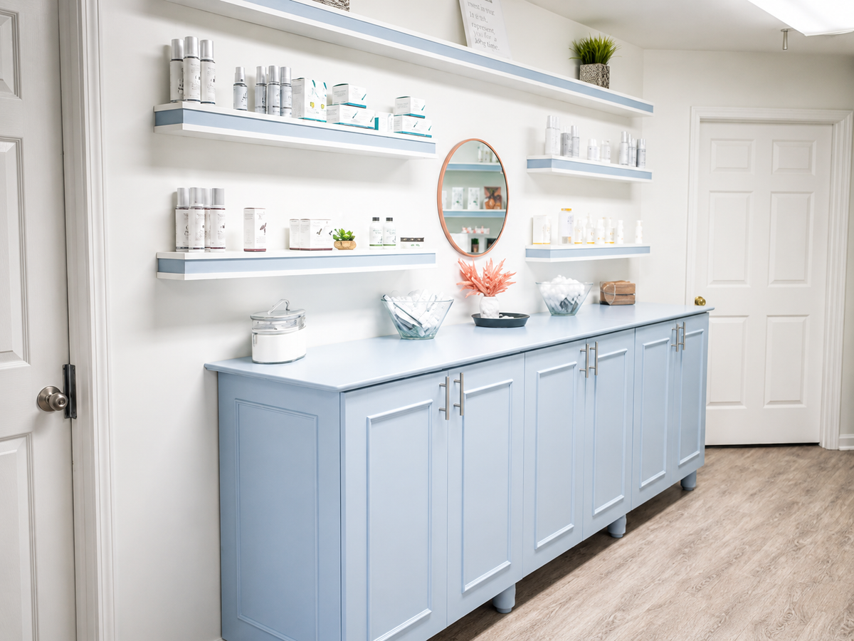 A light blue wooden cabinet with a matching countertop and floating shelves mounted on the wall, styled with skincare bottles, jars, and decorative items in a bright, clean room.