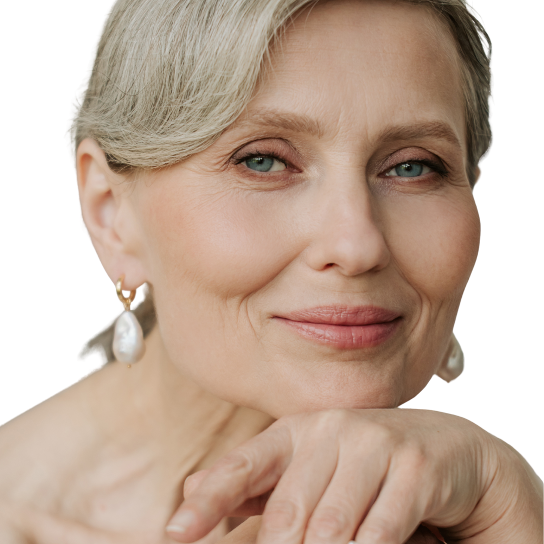 Close-up portrait of an older woman with short gray hair resting her chin on her hands, wearing small gold and pearl drop earrings against a plain white background.