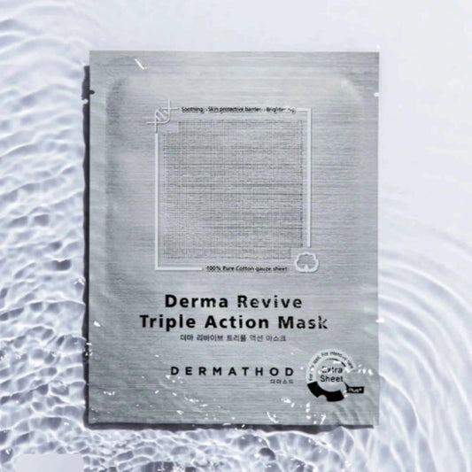 A single DermaThod Derma Revive Triple Action Mask sachet lies on a white surface with water ripples around it. The sachet is metallic silver-gray with black text and a small circular black-and-white certification-style seal near the bottom right.