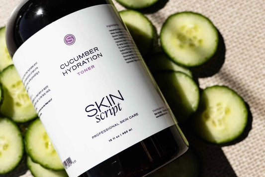A bottle of Skin Script Cucumber Hydration Toner with a white label, styled with fresh sliced cucumbers on a textured beige fabric background.