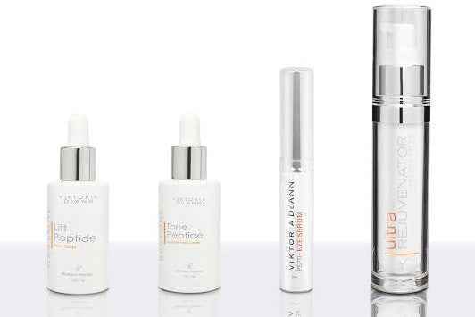 Four Vioneta Duvan skincare products arranged on a reflective white surface against a white background, including two white bottles with silver droppers, a slim white tube, and a tall clear bottle with silver detailing.