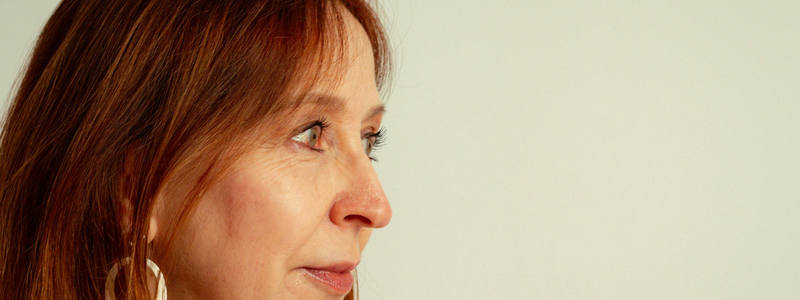 Close-up side profile of a woman with red-brown hair wearing a gold hoop earring against a plain light background.